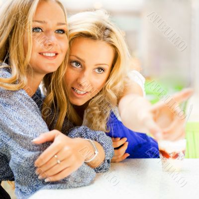 Two beautiful women drinking coffee and chatting at mall cafe.
