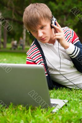 Student laying on grass and using laptop outside school