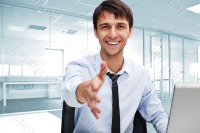 Businessman gives a handshake. Sitting near his laptop at his de