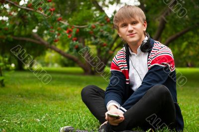 Student outside sitting on green grass and listening music via h