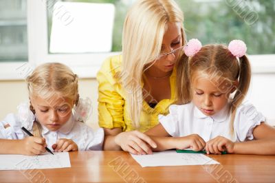 Teacher helps to little girls to make an exercises in classroom