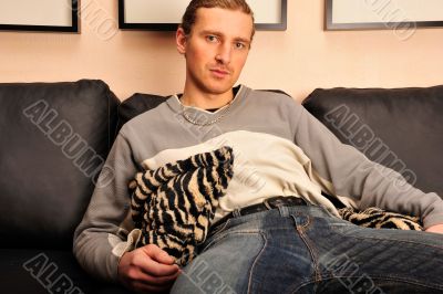 Happy young man sitting on sofa at home 