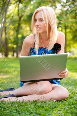 Beautiful student woman with a laptop sitting on green grass at 