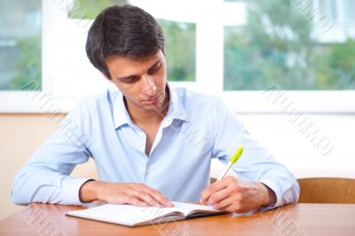 Businessman sitting indoors and writing plan in his diary