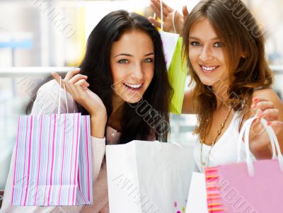 Two excited shopping woman resting on bench at shopping mall loo
