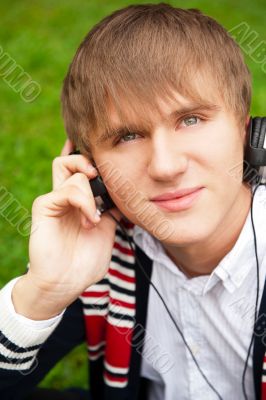 Student outside sitting on green grass and listening music via h Student outside sitting on green grass and listening music via h