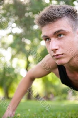 Portrait of young man full of attitude doing pushups on grass at