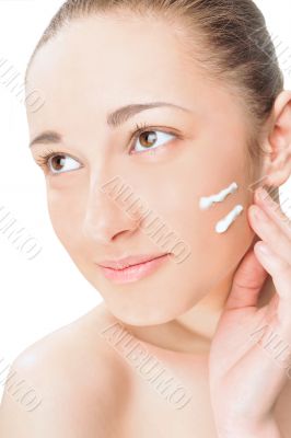Portrait of a beautiful young woman applying cream to her face.