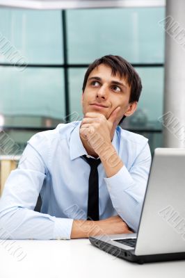 Portrait of a young business man sitting by his laptop in the of