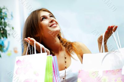 Shopping woman with lots of bags smiles inside mall. She is happ