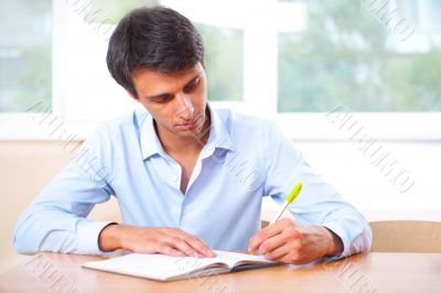 Businessman sitting indoors and writing plan in his diary