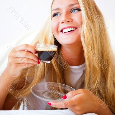 Smiling woman drinking a coffee lying on a sofa at home