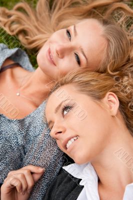 Two women whisperingá laughing and smiling at the city park. Sit