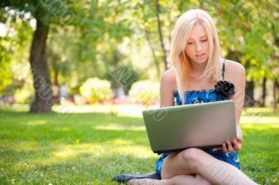 Beautiful student woman with a laptop sitting on green grass at 