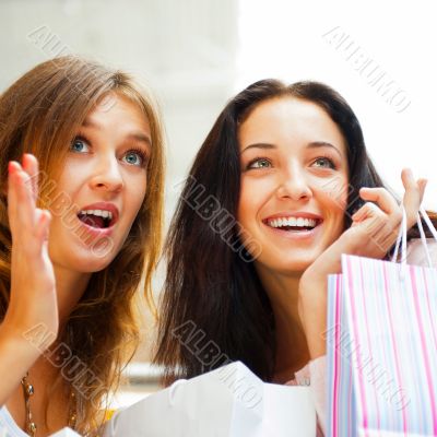 Two excited shopping woman together inside shopping mall. Horizo