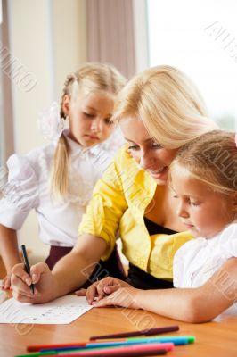 Young pretty teacher helping her little students in classroom