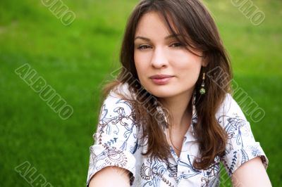 Closeup portrait of pretty young woman resting on grass and smil