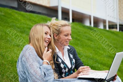Portrait of two smiling women using laptop on a green meadow at 