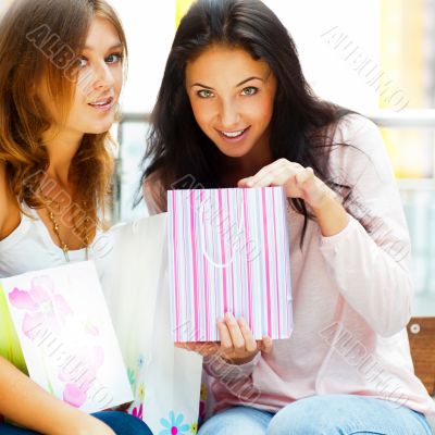 Two excited shopping woman resting on bench at shopping mall loo