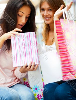 Two excited shopping woman resting on bench at shopping mall. Lo