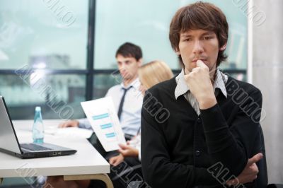 Portrait of a young business man sitting by his laptop in the of