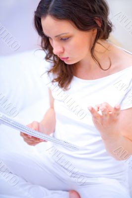 Young woman with a notebook studying at home sitting on bed. She