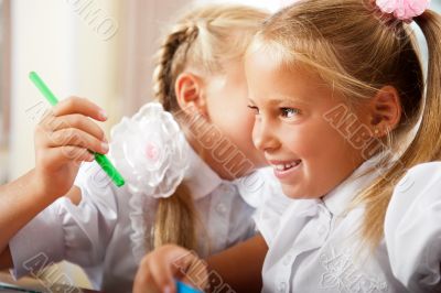 Two little girls gossip in classroom