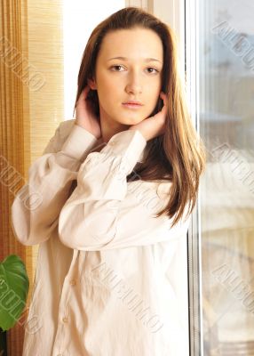 Portrait of cosy young girl standing near a window at home
