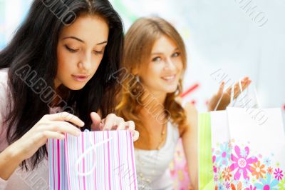 Two excited shopping woman resting on bench at shopping mall. Lo