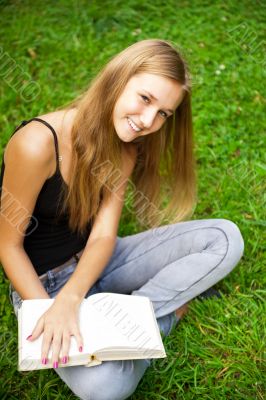 Beautiful female student outdoors with a book at campus park