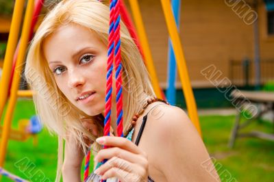Portrait of pretty young woman swinging on playground at park an