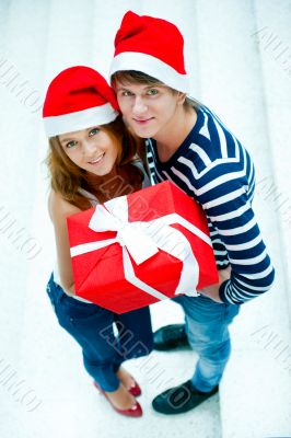 Young happy couple in Christmas hats standing together and holdi