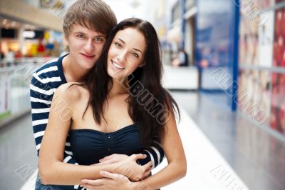 Portrait of young couple embracing at shopping mall and looking 