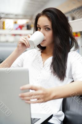 Portrait of a beautiful young woman working on laptop and drinki