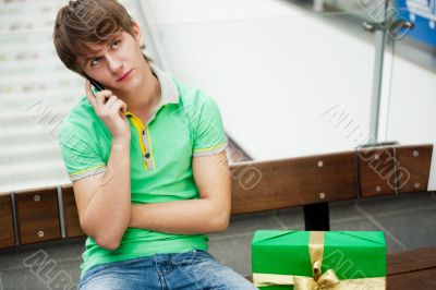 Portrait of young man inside shopping mall with gift box sitting