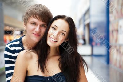 Portrait of young couple embracing at shopping mall and looking 