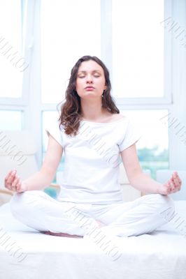 Young woman meditating with closed eyes in bright bedroom sittin