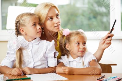 Young pretty teacher helping her little students in classroom