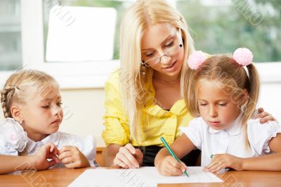 Teacher helps to little girls to make an exercises in classroom