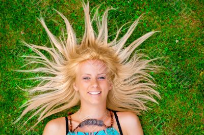 Young woman laying on green grass with hair like a sun around he