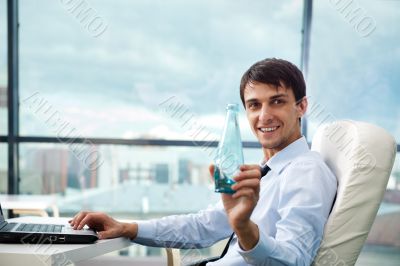 Young business man drinking water sitting relaxed on armchair at