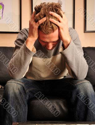 Closeup portrait of young man sitting on sofa with headache