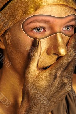 Closeup portrait of young woman in golden paint closing her mout