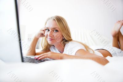 Smiling woman using a laptop while lying on her bed