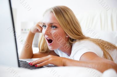 Smiling woman using a laptop while lying on her bed and playing