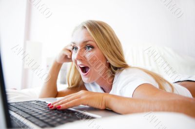 Smiling woman using a laptop while lying on her bed and playing