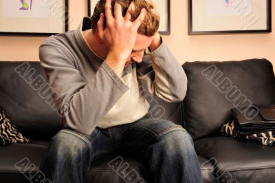 Closeup portrait of young man sitting on sofa with headache