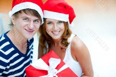 Young happy couple in Christmas hats standing together and holdi