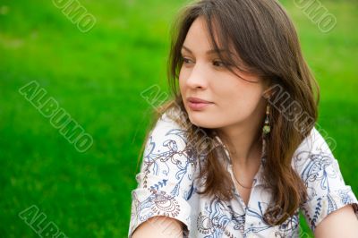 Closeup portrait of pretty young woman resting on grass and smil