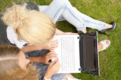 Portrait of two smiling women using laptop on a green meadow at 